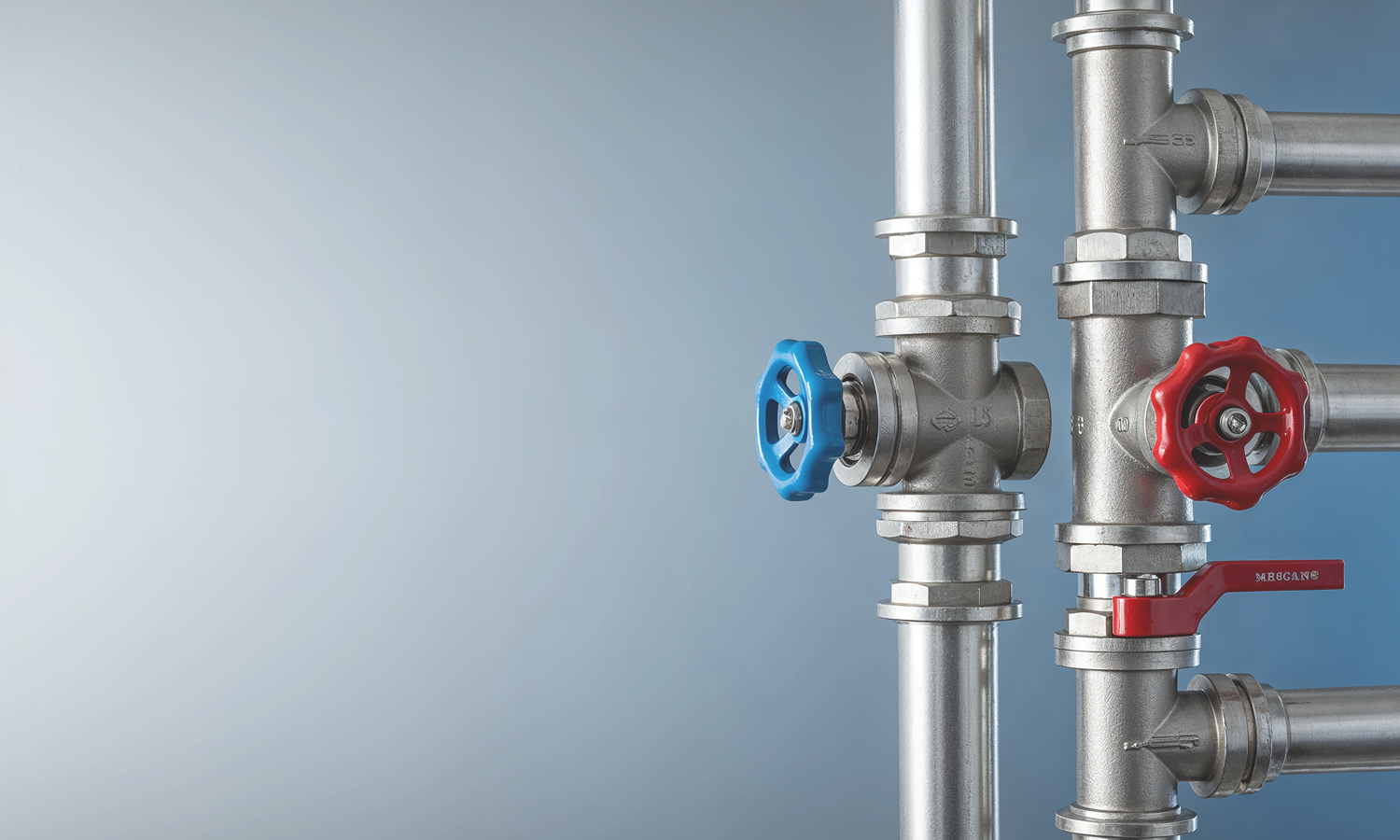 Close-up of metal pipes with red and blue valve handles against a blue-gray background.